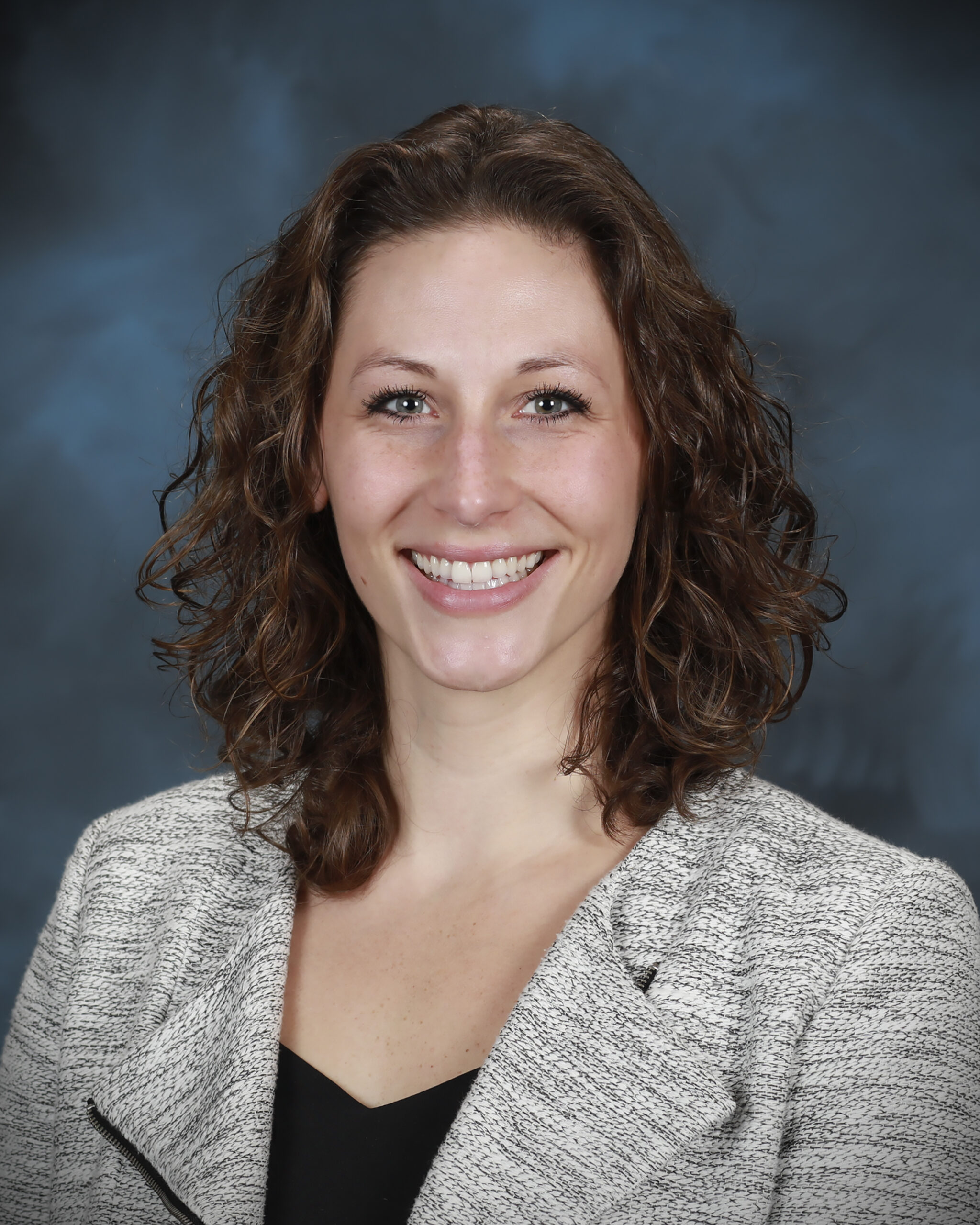 Innovation Crossroads fellow Megan O'Connor is posing for a photo in a grey blazer with curly red hair