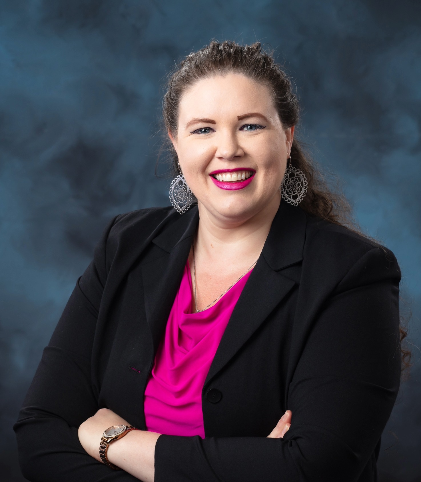 ORNL researcher Anne Campbell is posing for a photo in a bright pink shirt and black jacket with a dark grey cloudy backdrop