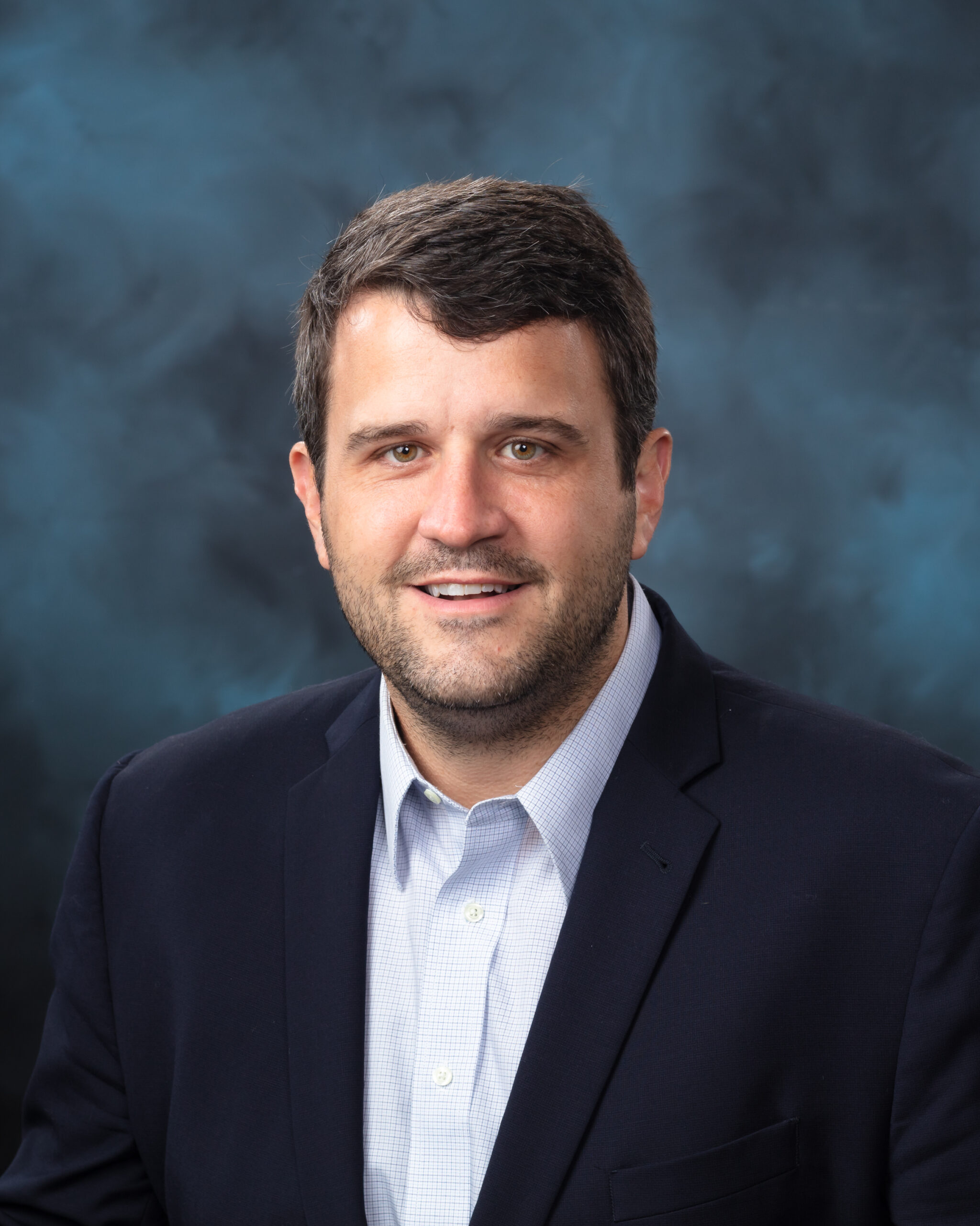 ORNL chemist Benjamin Manard is posing for a photo with a light blue and navy background