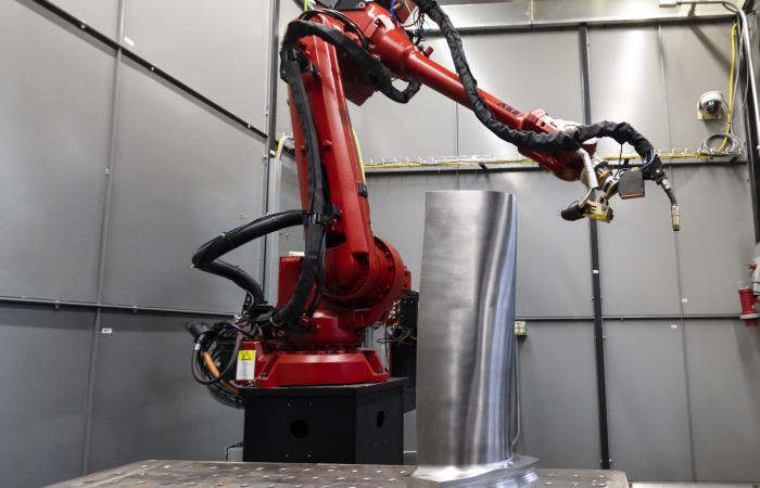 Large red robotic arm used for additive manufacturing to complete steam turbine blade