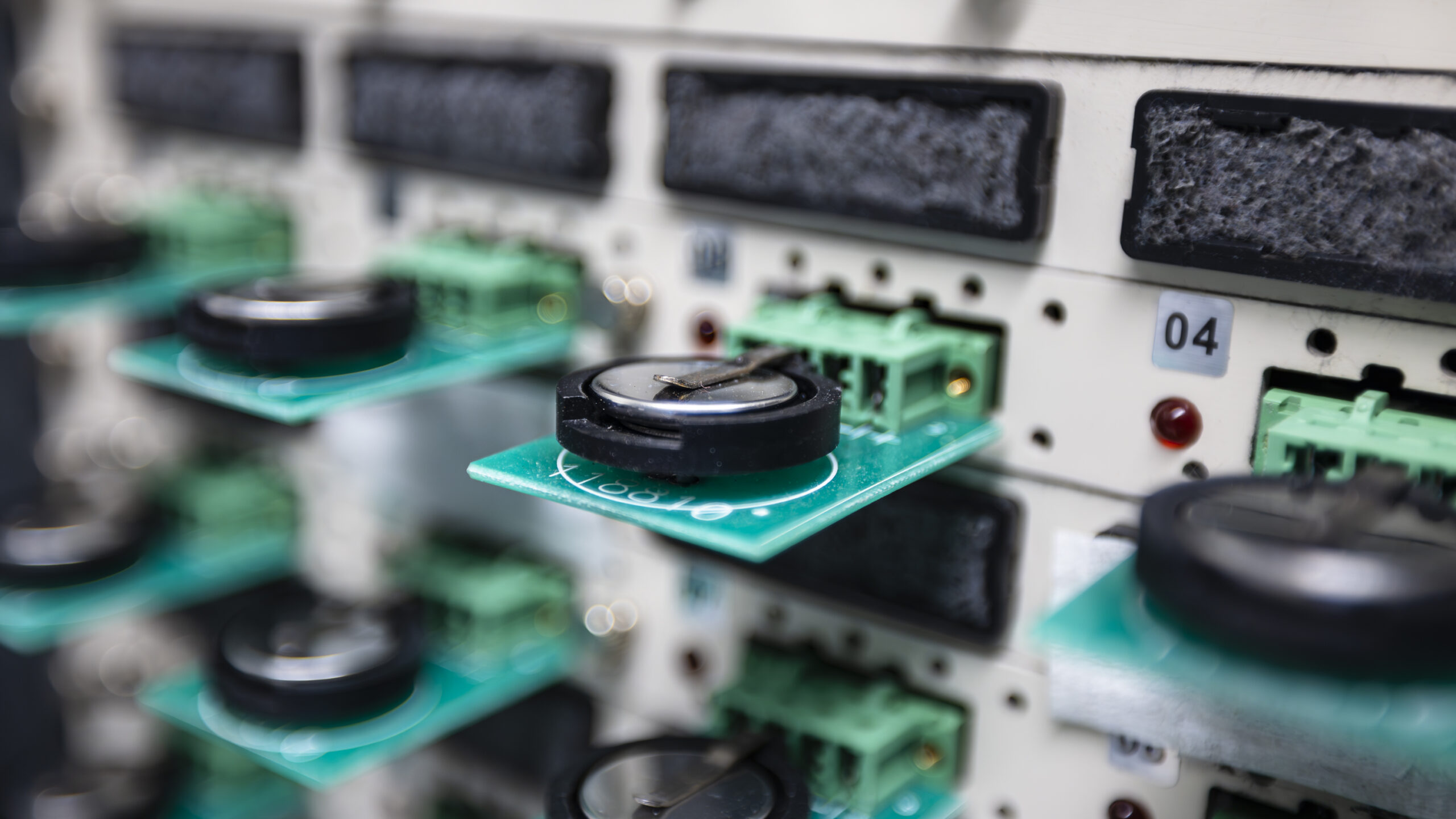 The picture is a close up of a coin cell battery being tested, with green panels on the wall holding the black, circular battery. 