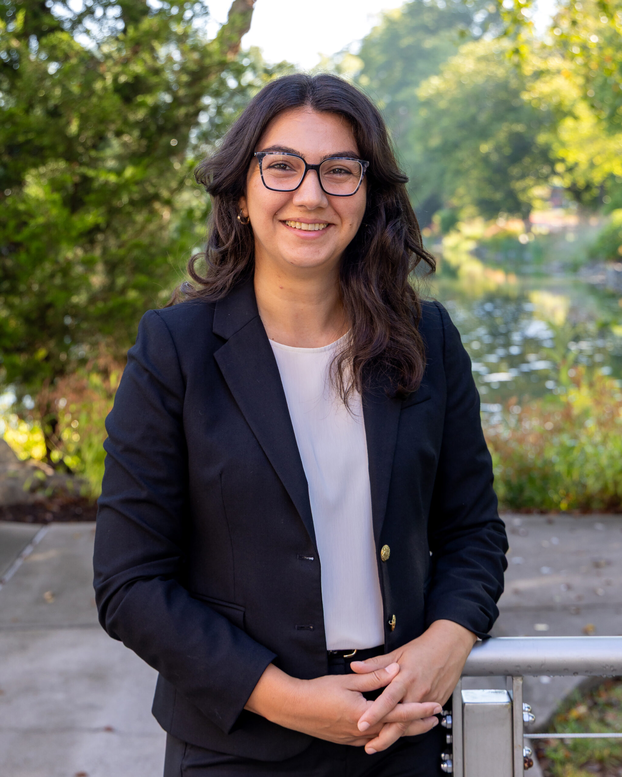 ORNL analyst is wearing a black blazer and glasses outside with her arms crossed smiling for a photo.