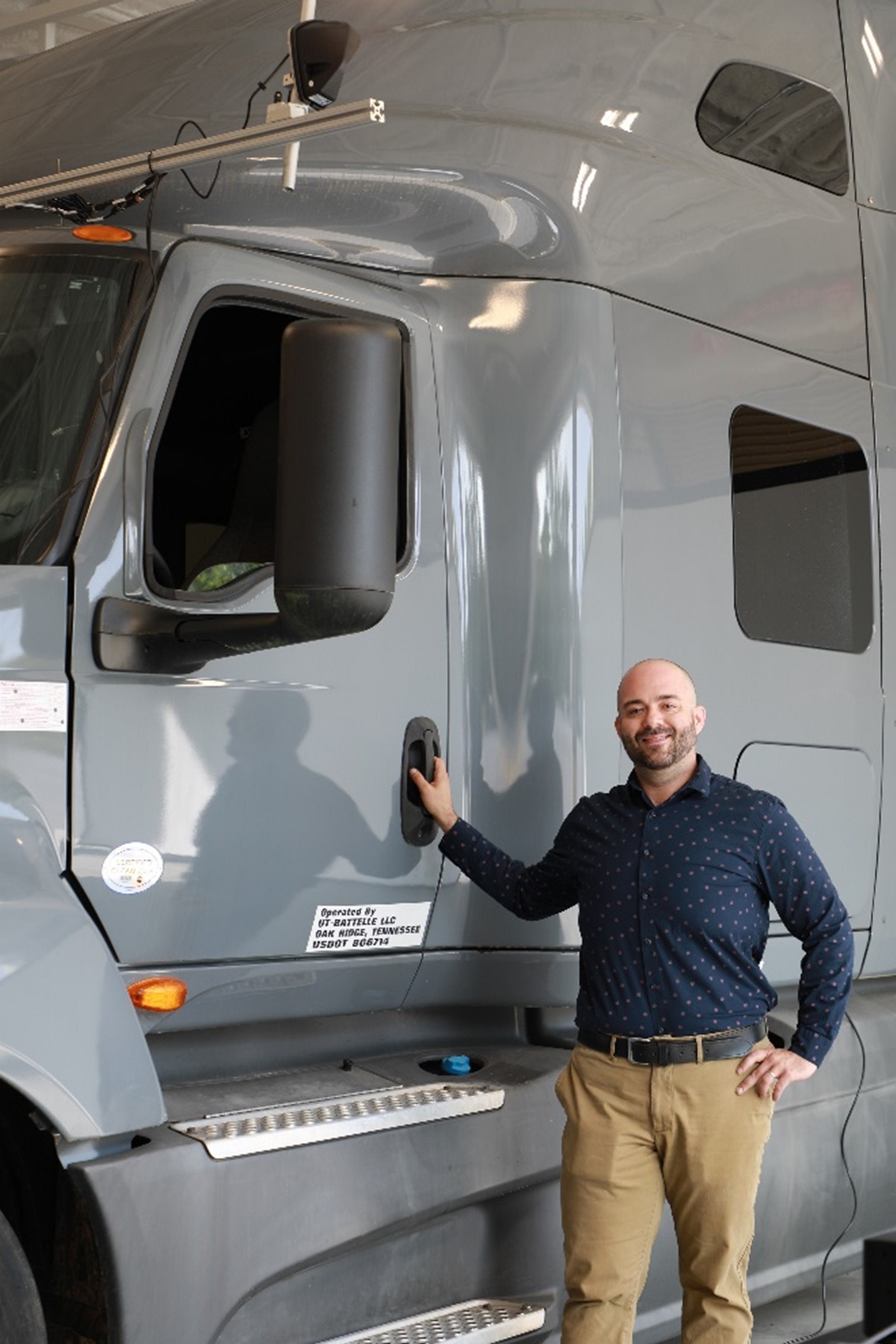Man is standing outside of a grey semi-truck posing for a photo