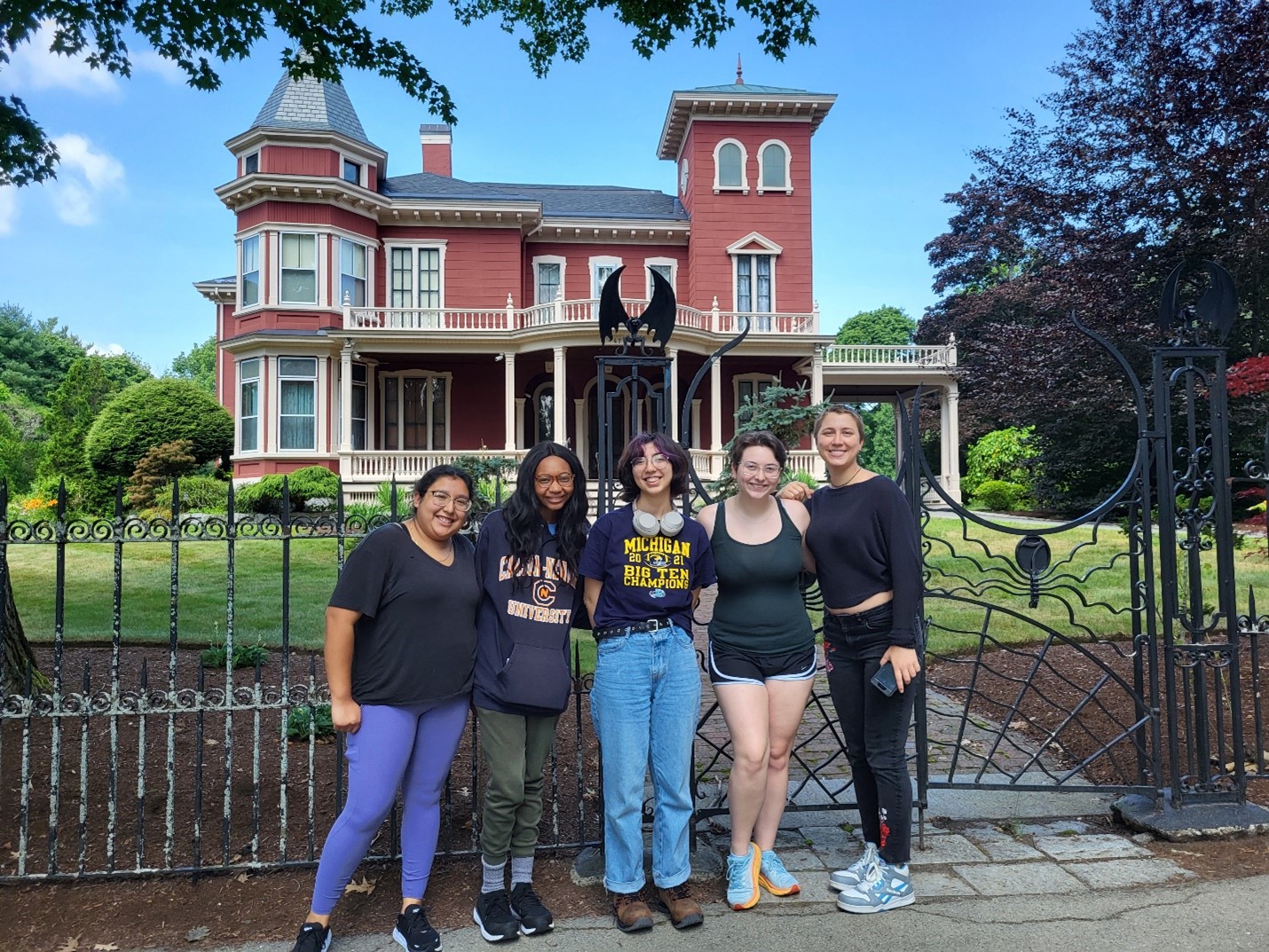 Five girls stand outside of a red brick building with iron gate out front, Stephen King's house.