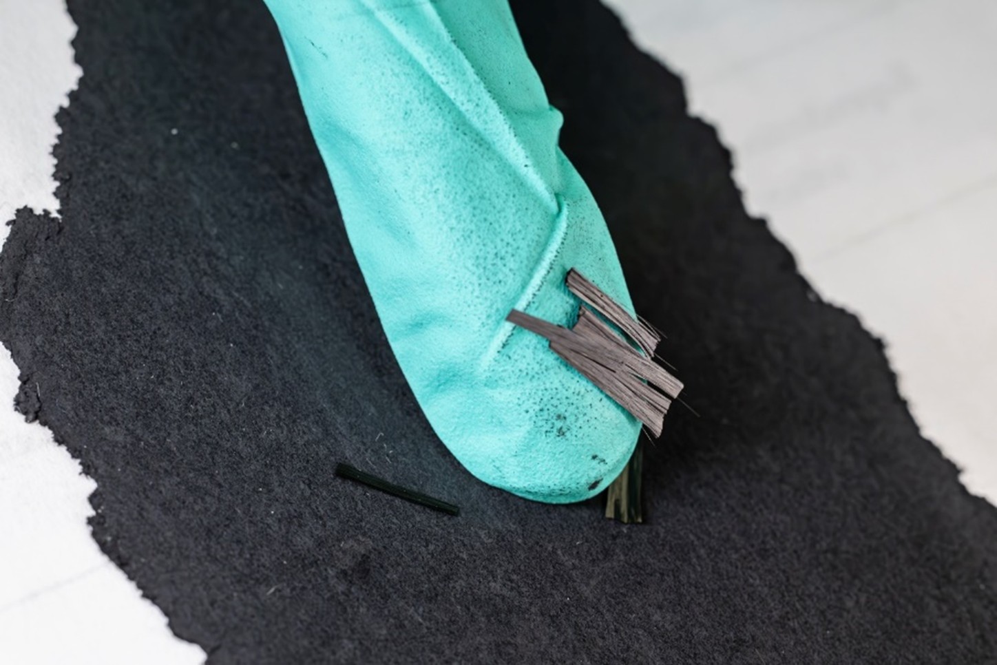 Small thin shreds are called "carbon fiber snippets" laying on the finger tip of a blue glove
