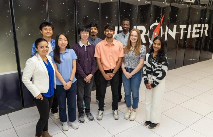 Group of 9 students standing in front of the Frontier Supercomputer