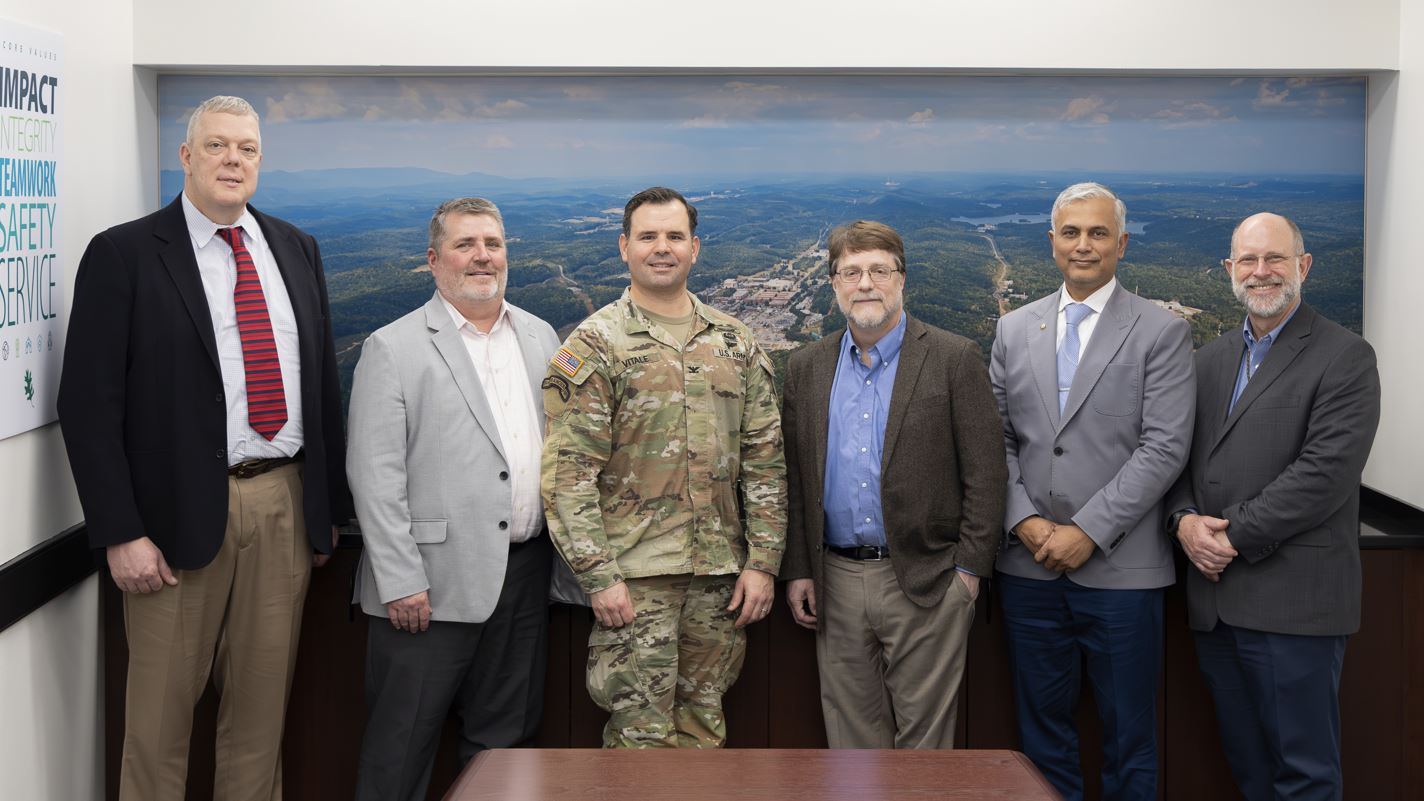 Six men standing side by side in conference room posing for a photo with Stephen Streiffer and a US Army personal in the middle