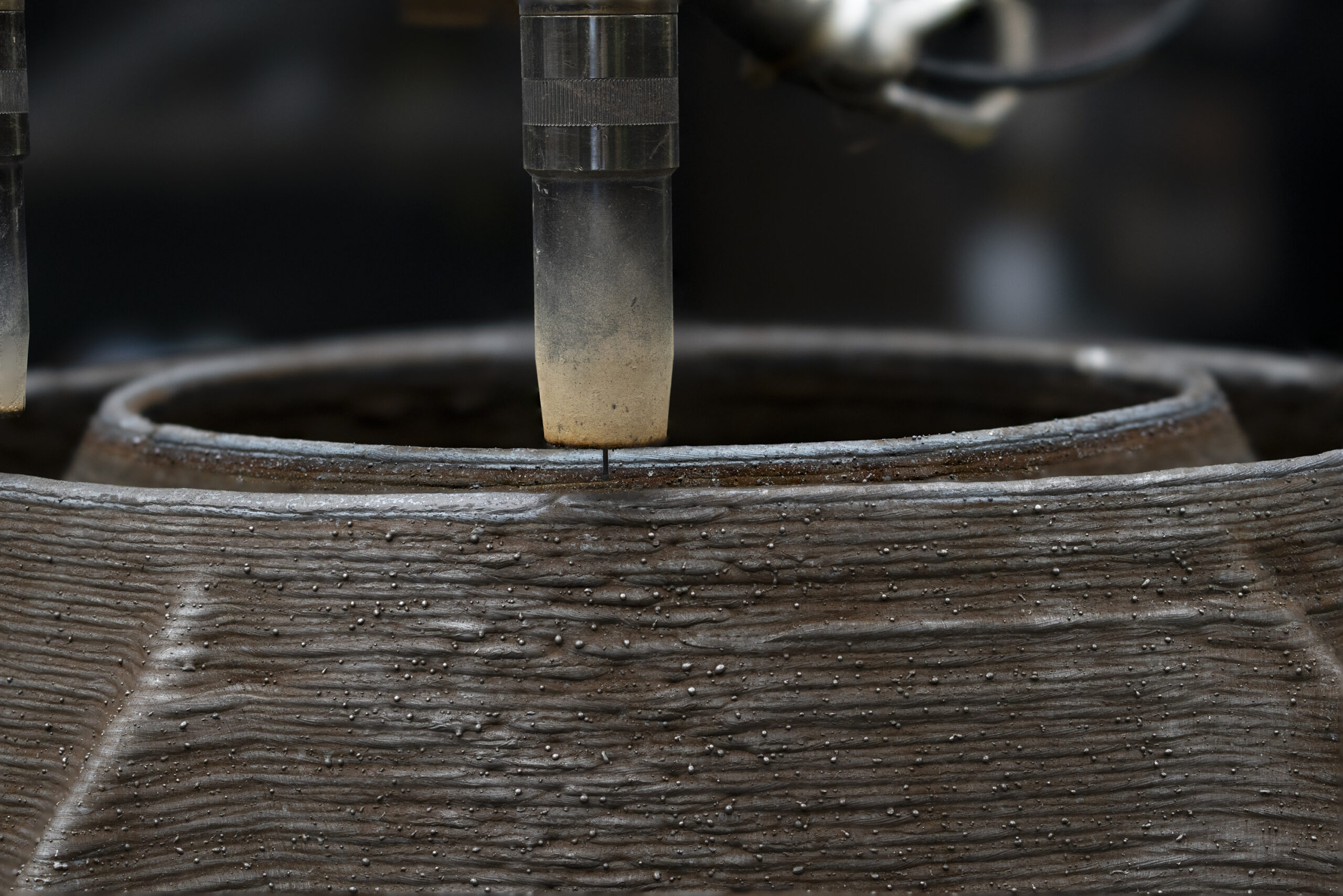 Close-up of a 3D printing nozzle depositing metal material onto a layered cylindrical structure.