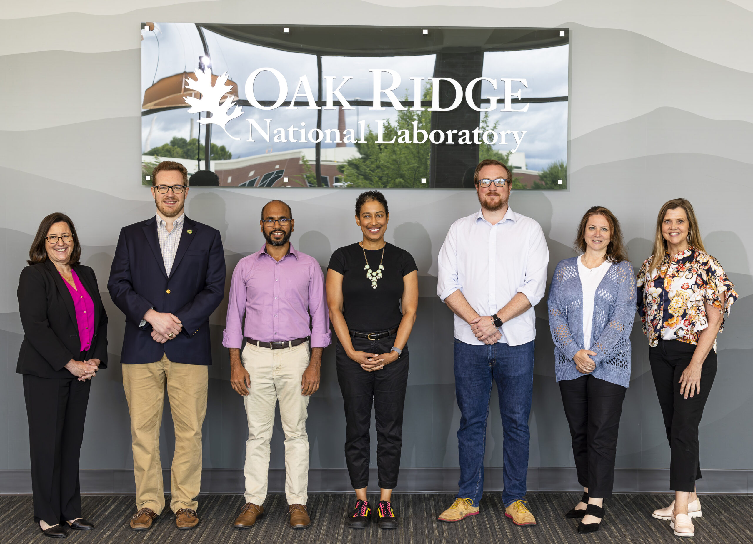 Seven staff members pose beneath an Oak Ridge National Laboratory sign in a lobby.