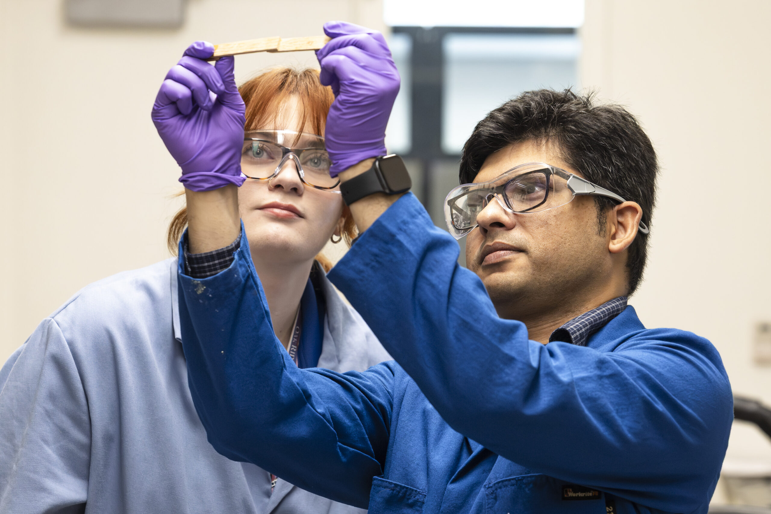 Two researchers are holding a material sample, looking up to the light