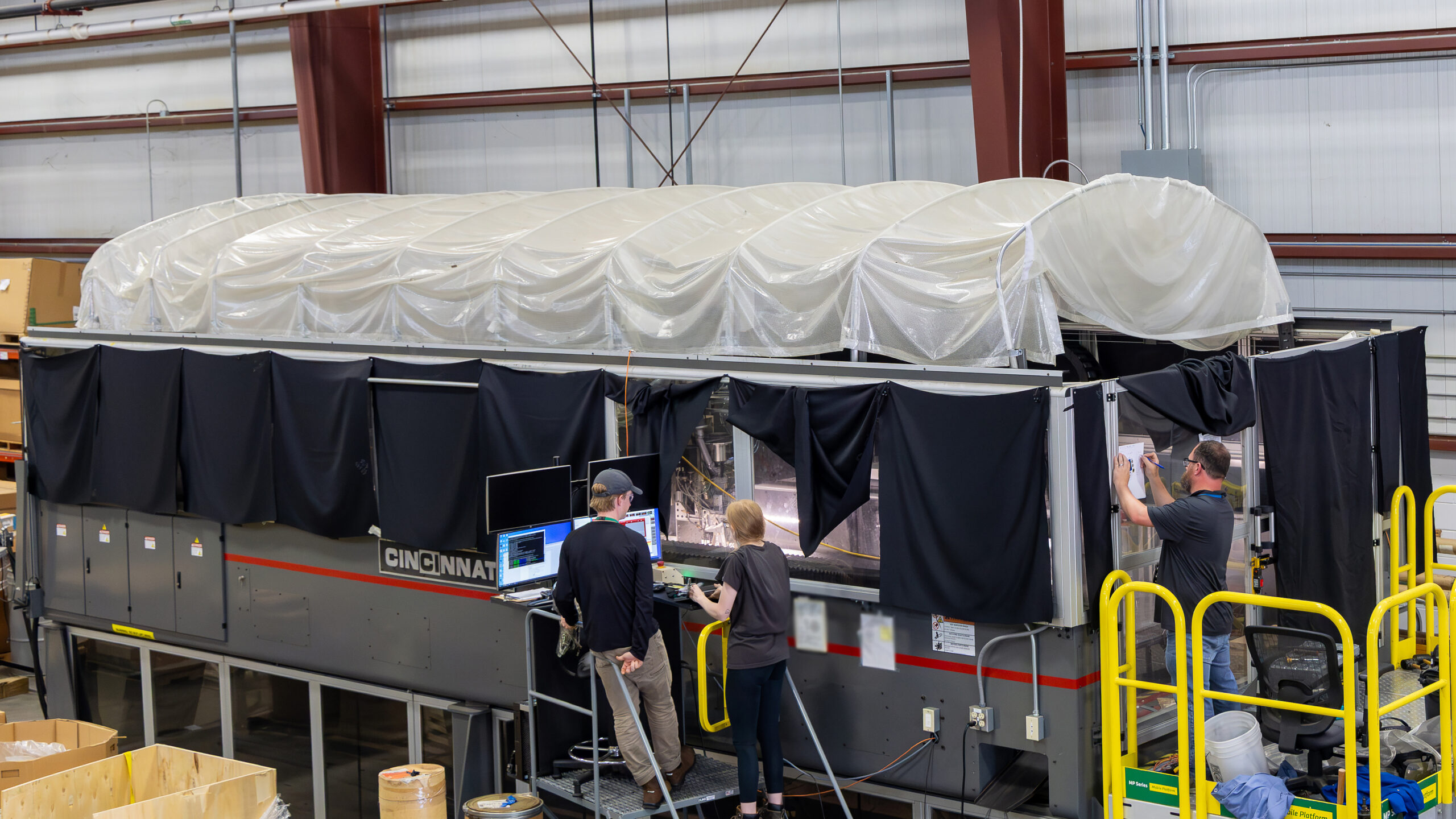 Researchers monitor a large-scale 3D printing system inside an industrial manufacturing facility.