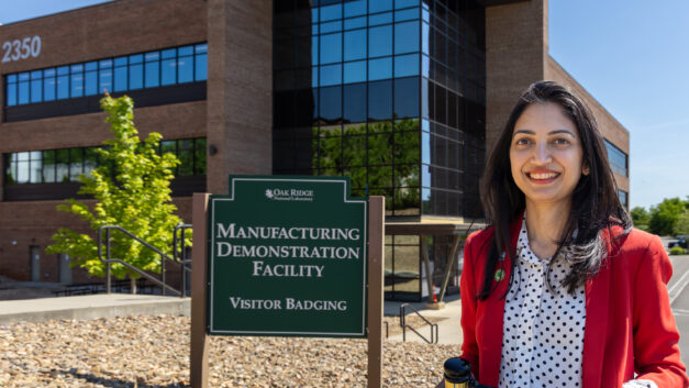 Sana Elyas stands outside ORNL’s Manufacturing Demonstration Facility holding a ceremonial gavel awarded for her election as SAMPE North America president.