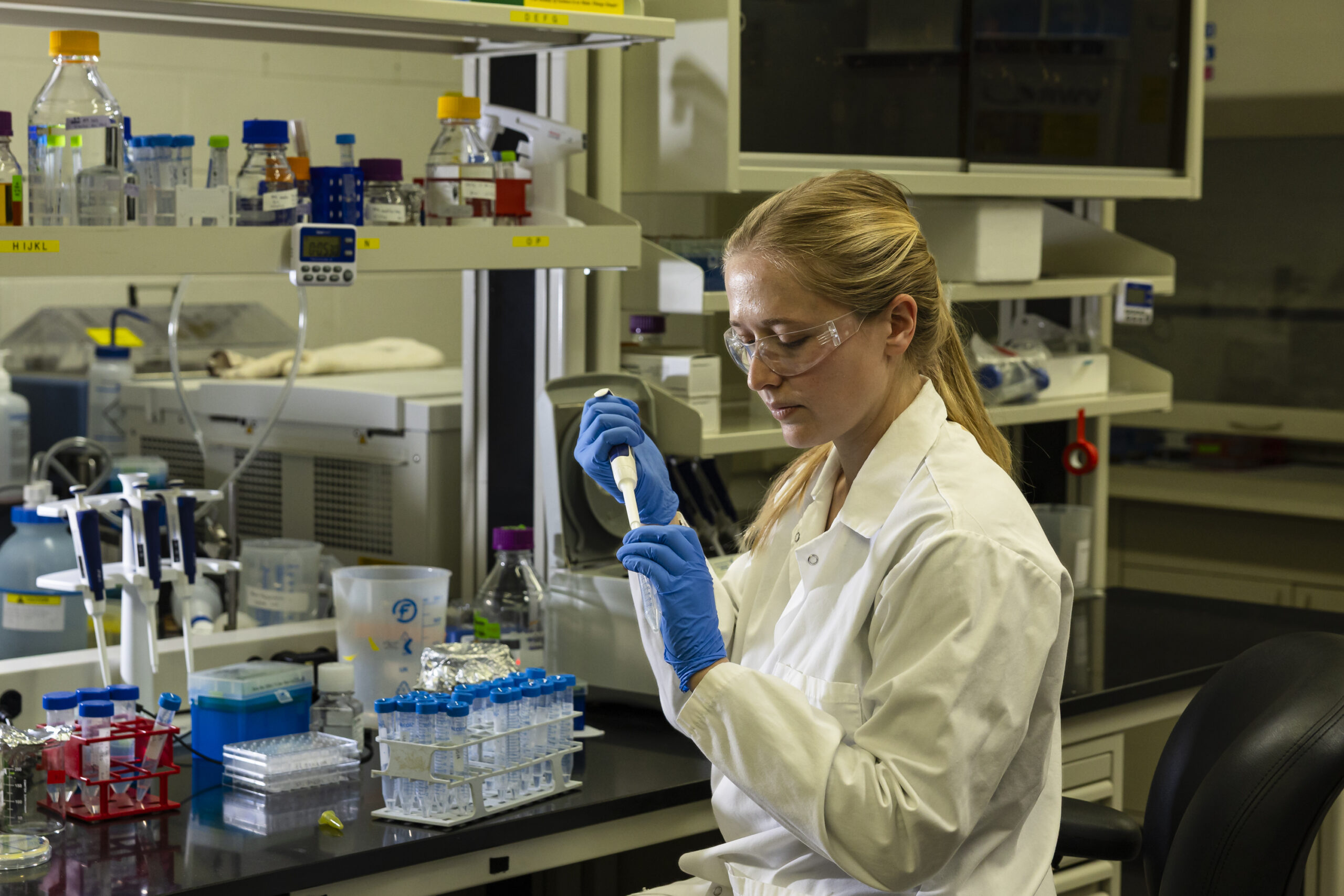 Scientist wearing safety glasses and gloves carefully pipetting liquid in a laboratory workspace