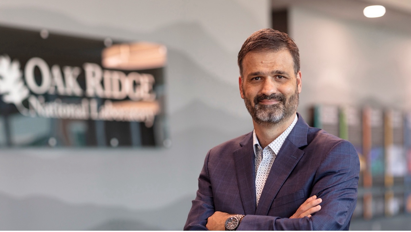 Business professional smiling in front of an Oak Ridge National Laboratory sign.