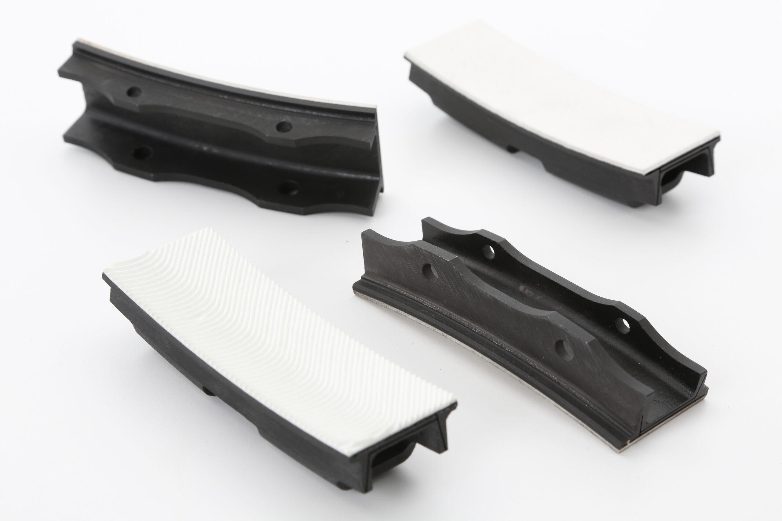 Four curved industrial components, black and white, displayed on a white surface.