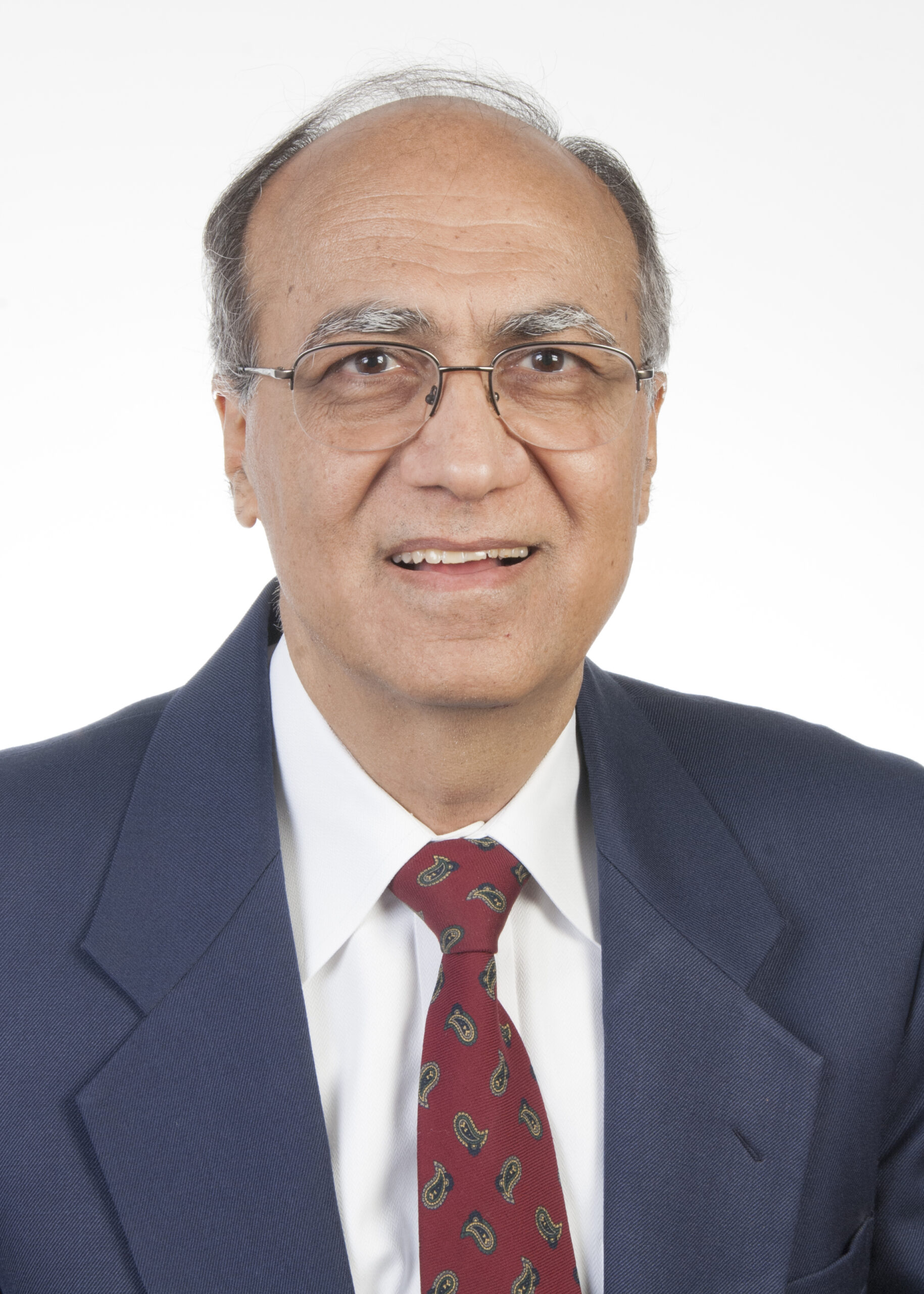 Headshot of a man in glasses wearing a suit and red patterned tie, smiling against a plain background.