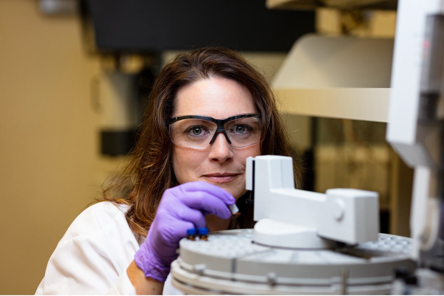 Scientist in safety glasses and gloves adjusting a sample on lab equipment