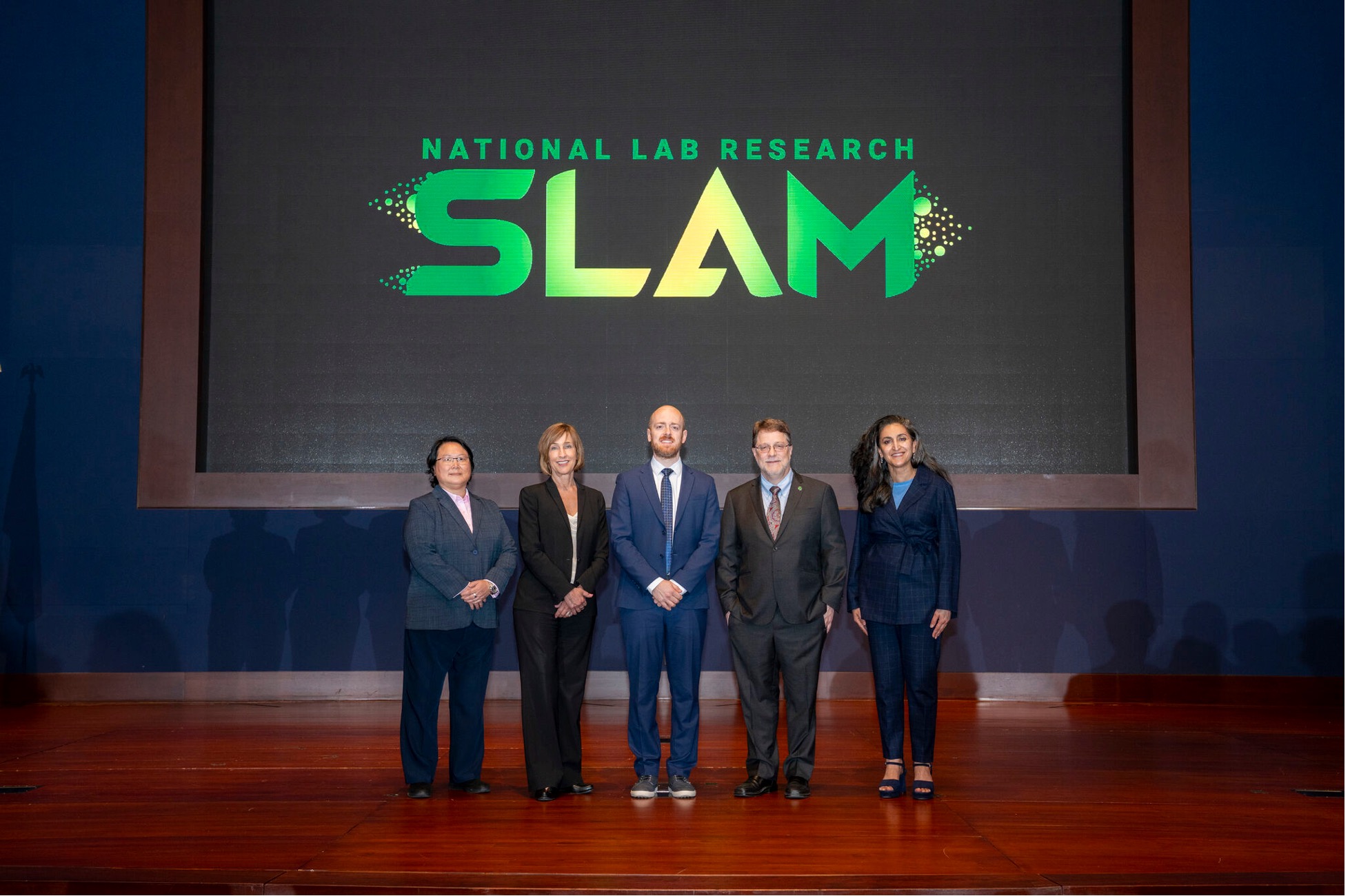 Five people stand on a stage beneath a large "National Lab Research SLAM" display.