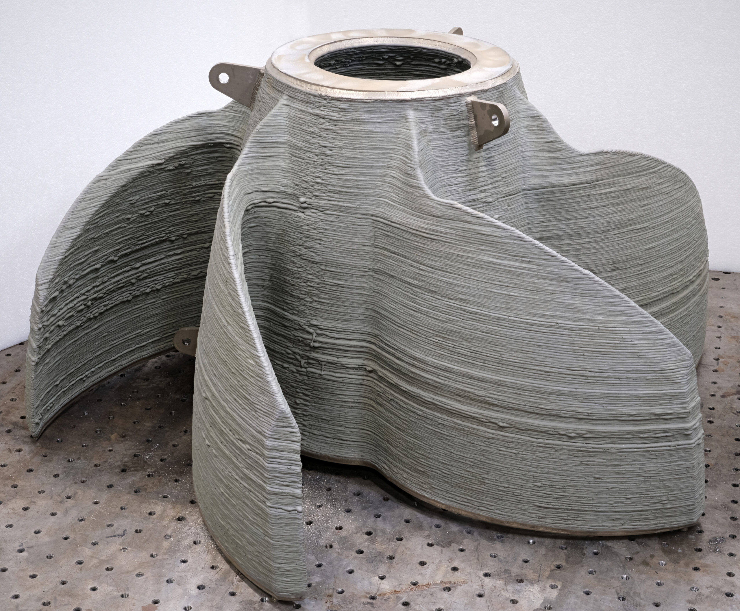 Large gray 3D-printed concrete structure with curved fin-like walls and visible layered texture on a metal worktable.