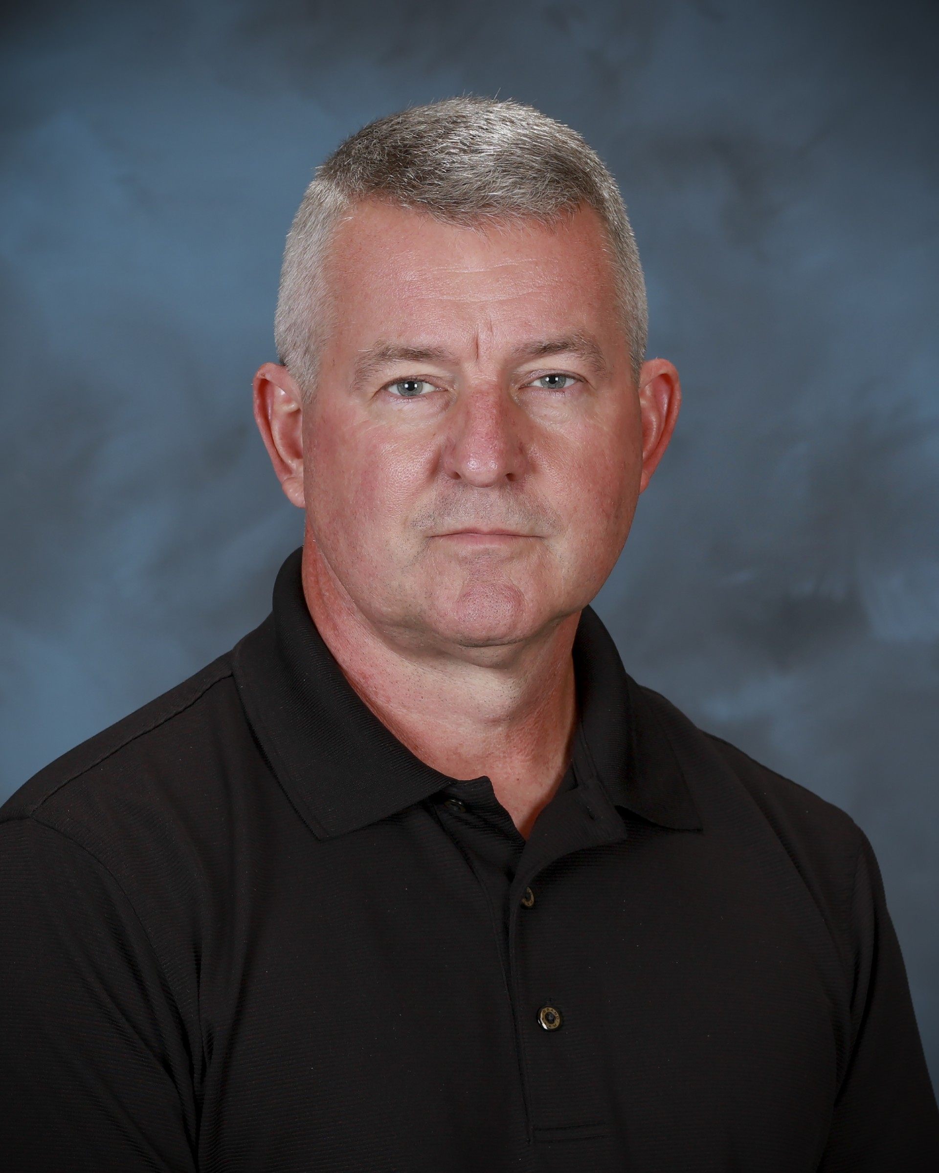 Headshot of a man in a black polo shirt against a neutral background.
