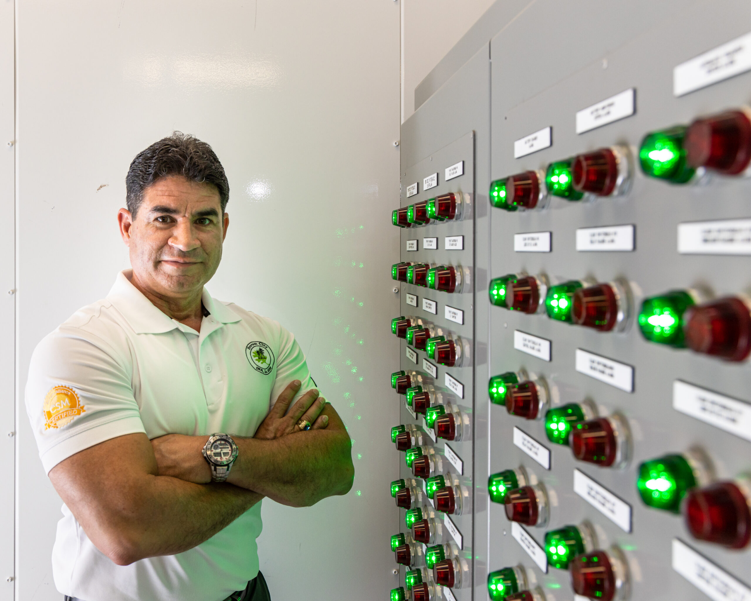 A man stands with arms crossed next to an energy system control panel