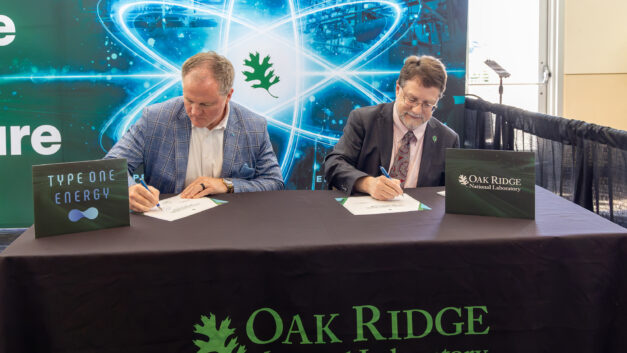 Matt Miles and Stephen Streiffer sign documents at a table during an MOU signing ceremony at the NOW Conference.