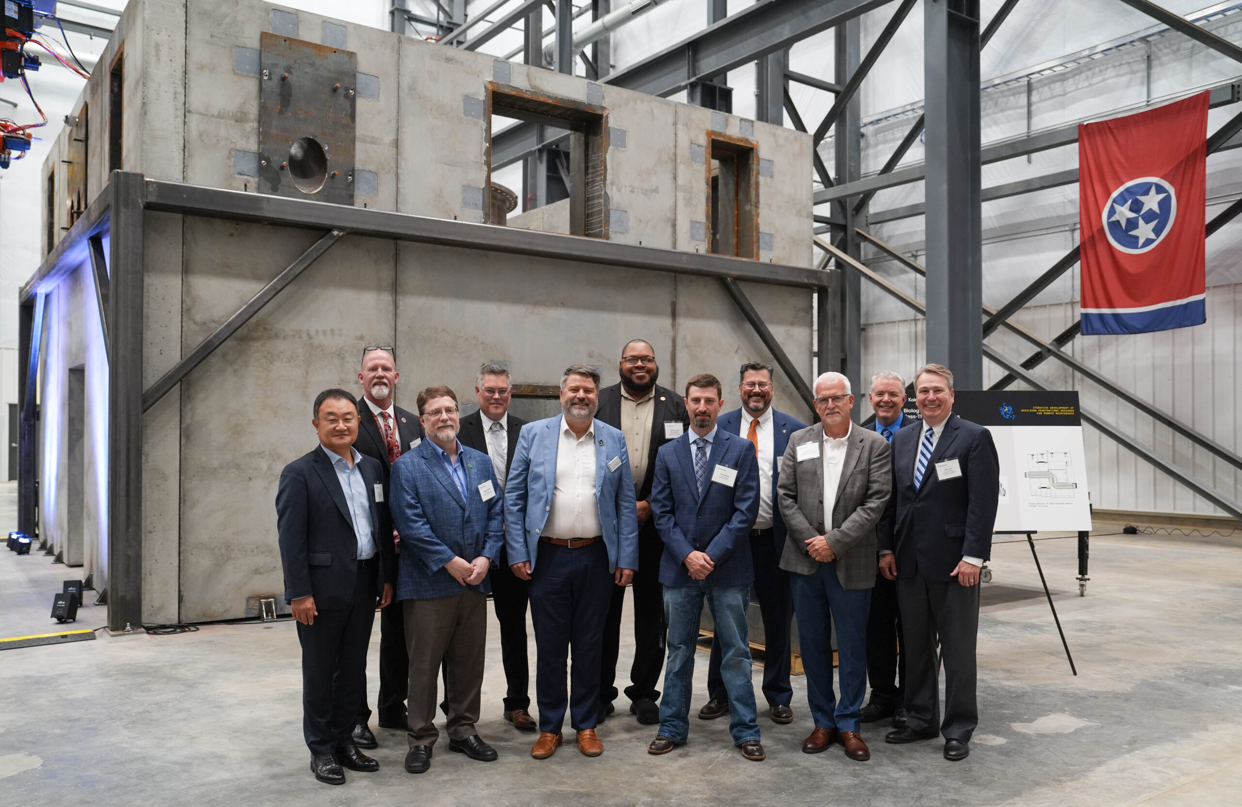 Kairos Power representatives and partners pose in front of a large concrete test structure at a Tennessee facility.