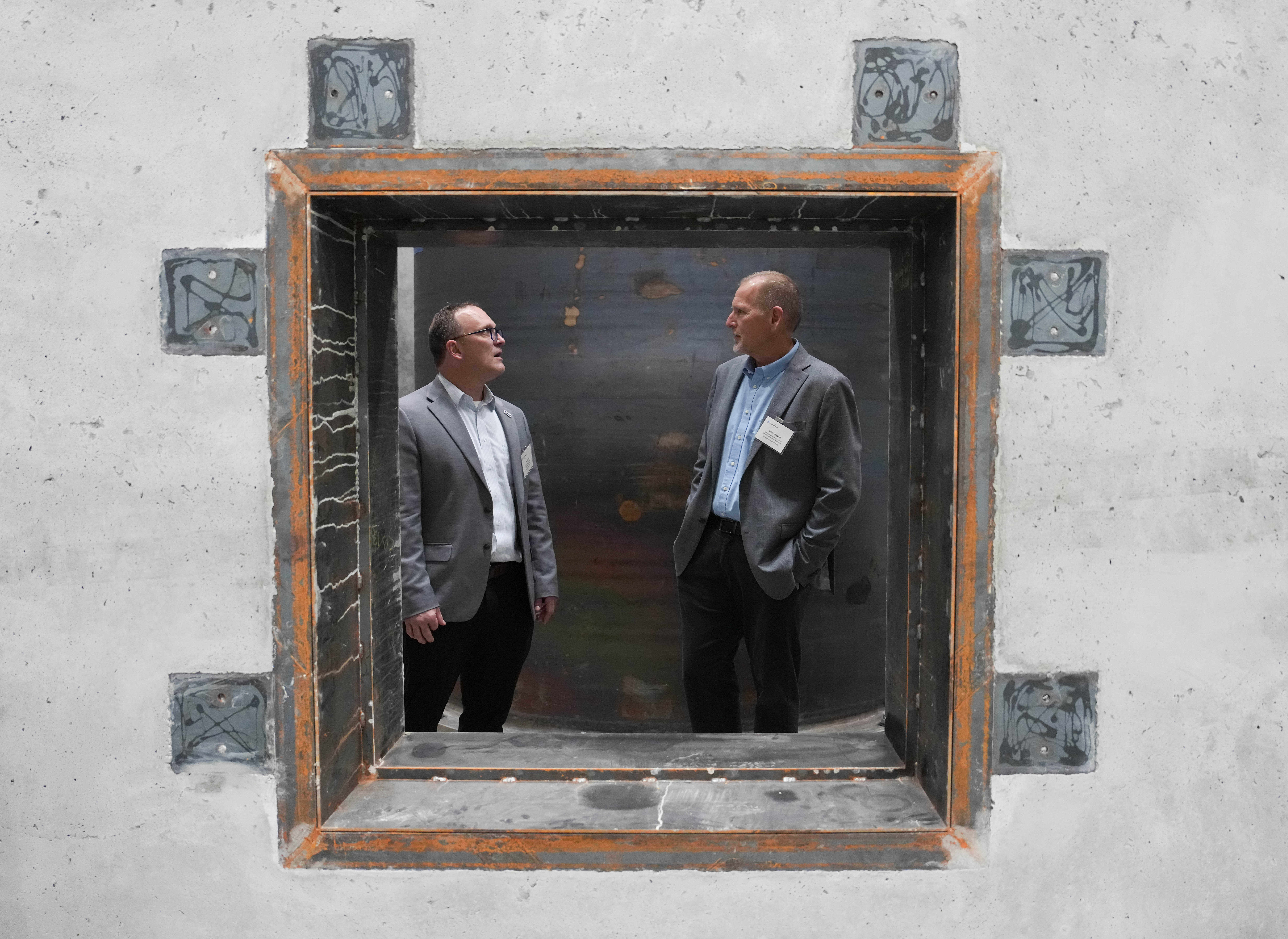 Two men talk while standing inside an opening in a large concrete test structure.