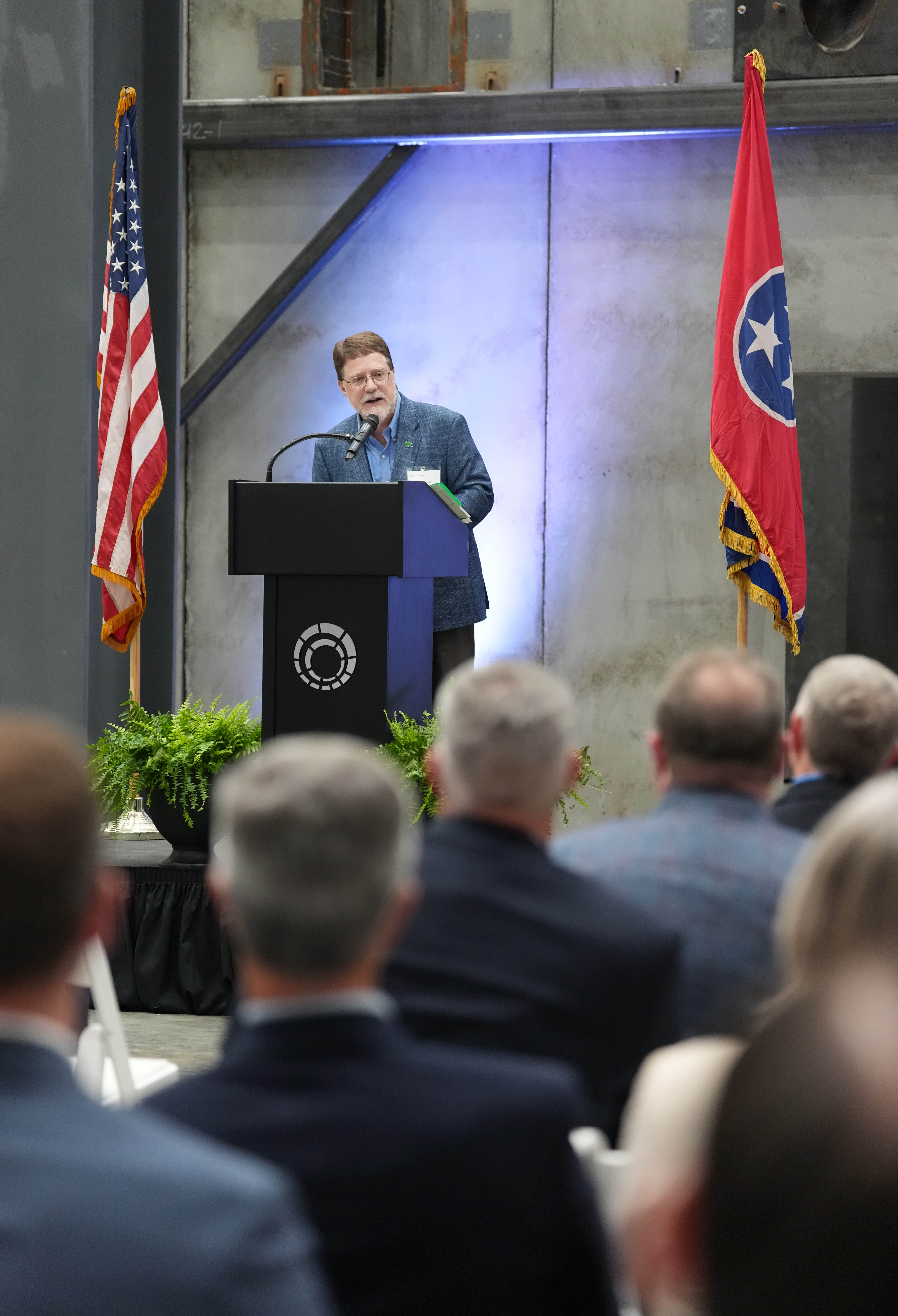 A speaker addresses an audience at a podium between the U.S. and Tennessee flags.