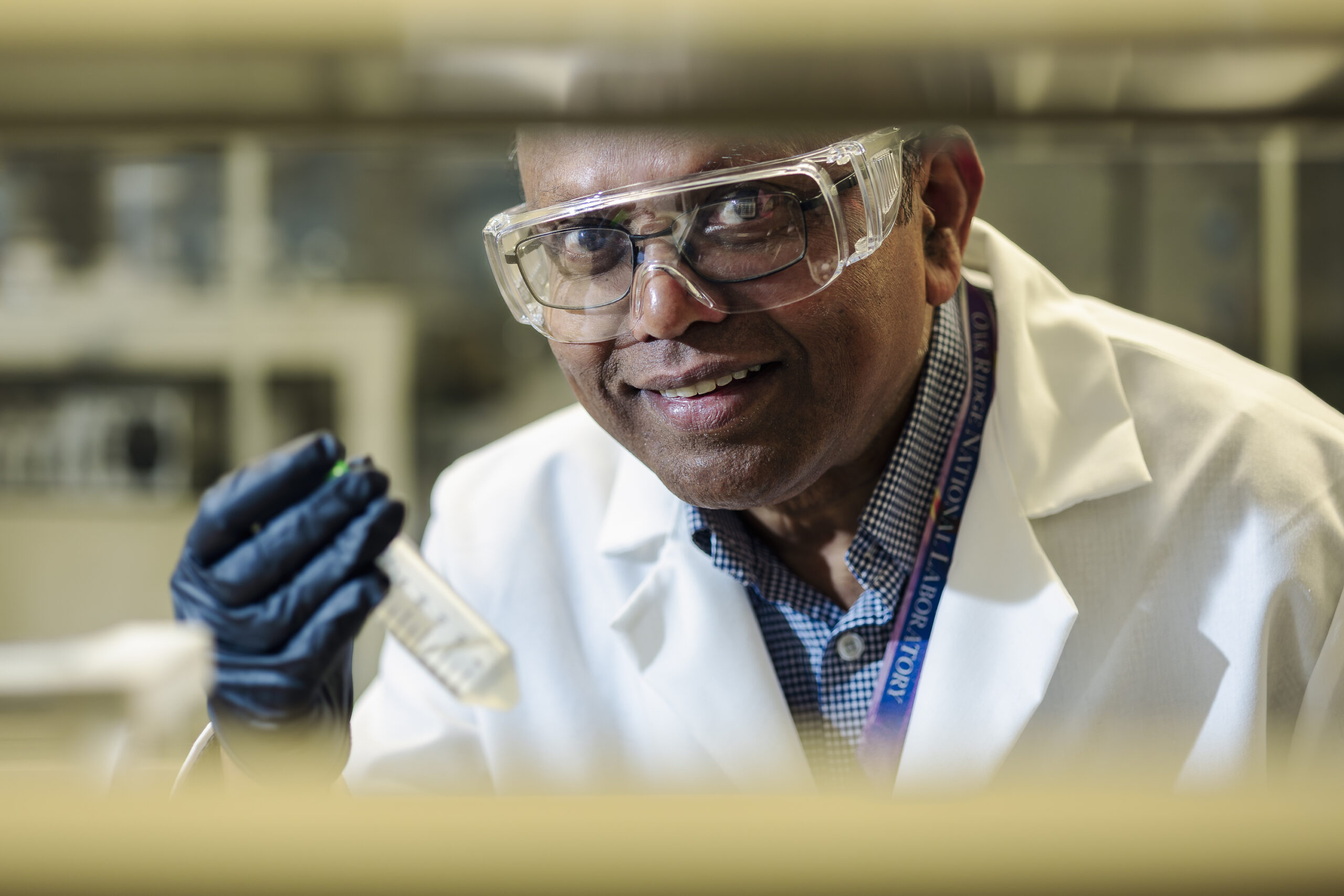 Scientist wearing safety goggles and gloves examines a sample tube in a laboratory.