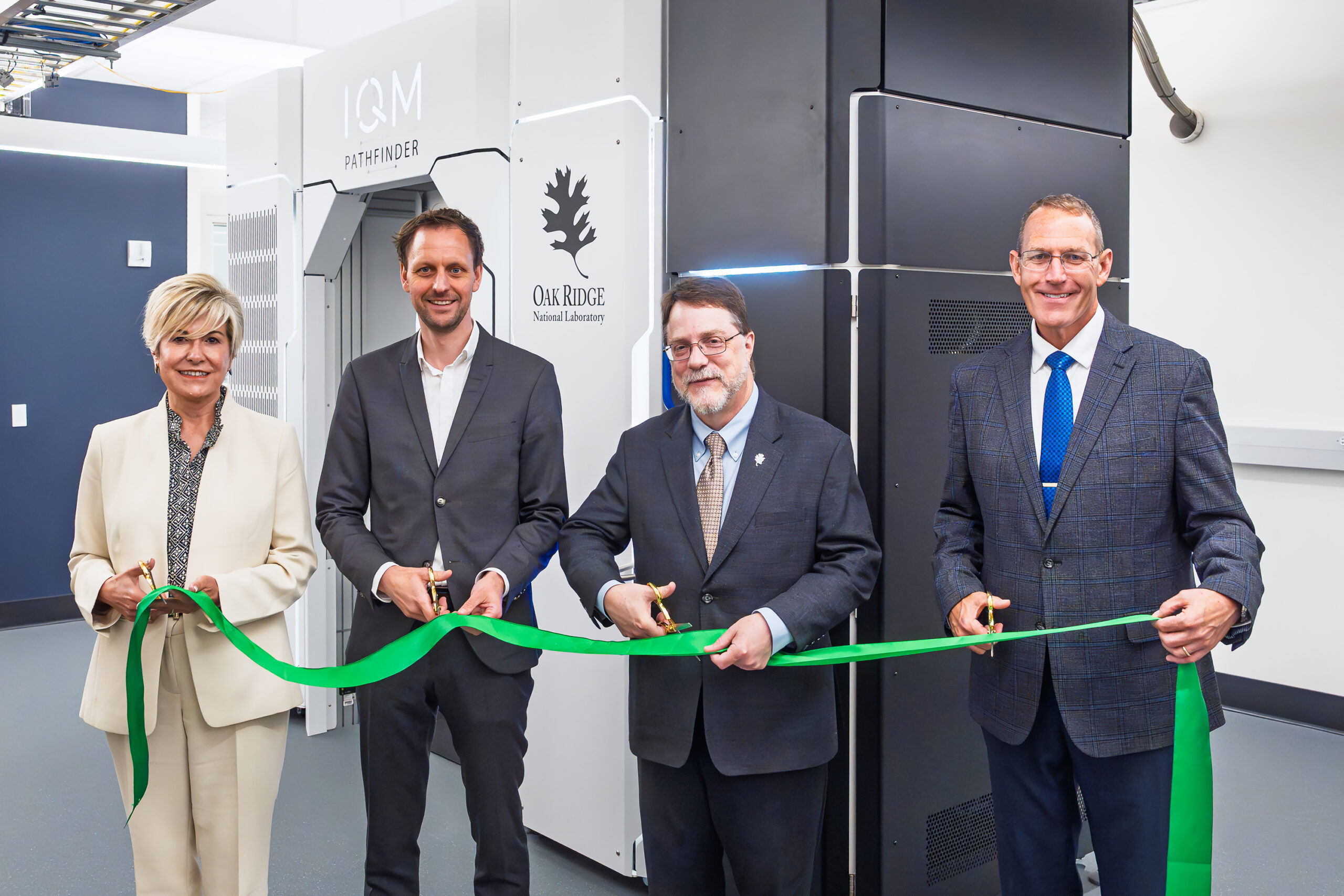 Four people participate in a ribbon-cutting ceremony in front of the IBM Pathfinder quantum computer at Oak Ridge National Laboratory.