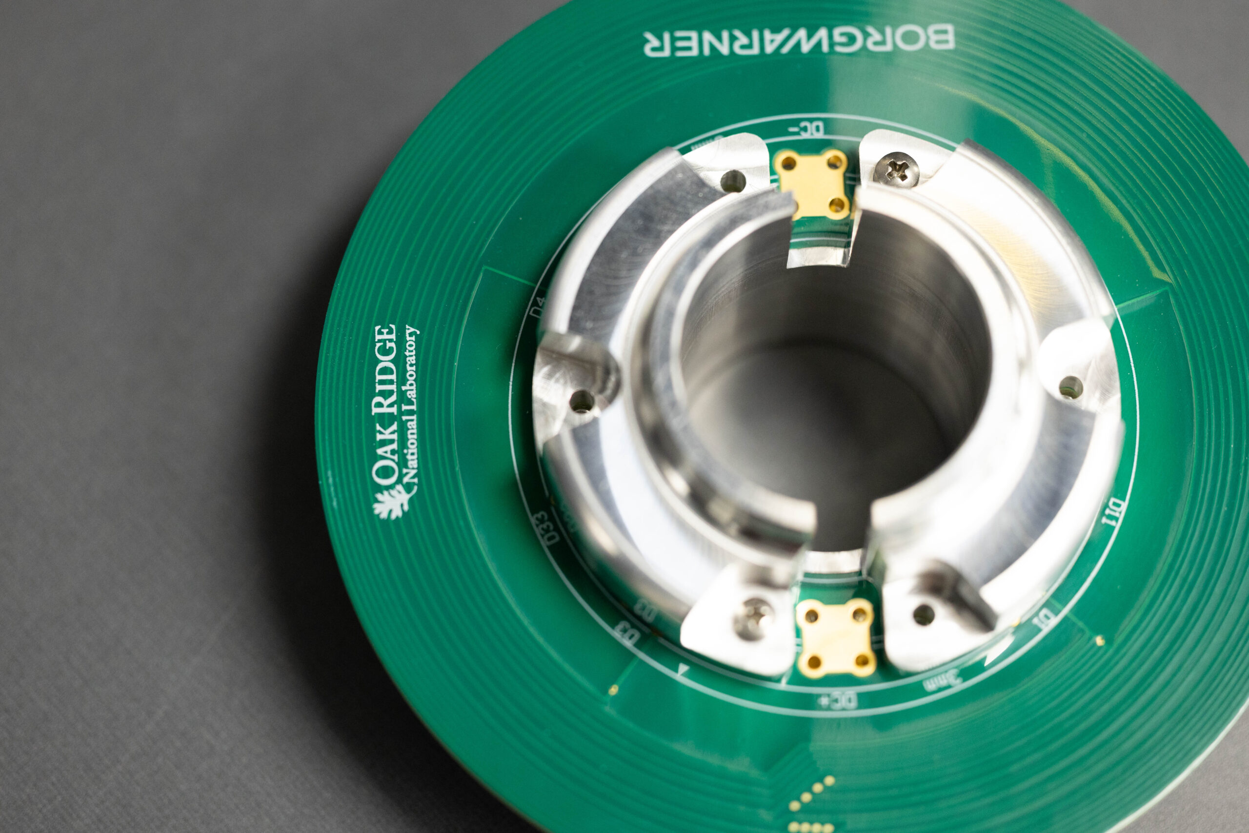 Close-up of a circular green circuit board with a metallic brushless motor component, featuring Oak Ridge National Laboratory branding.