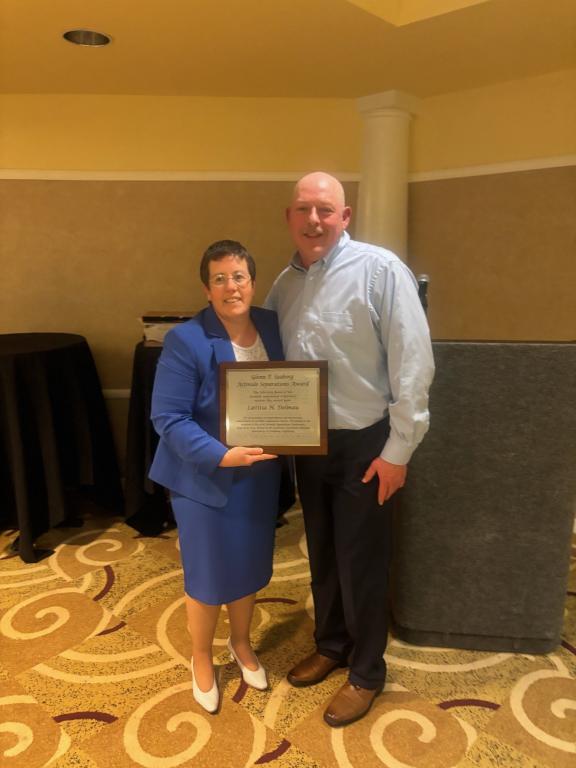 Two people pose with an award plaque at a recognition event.