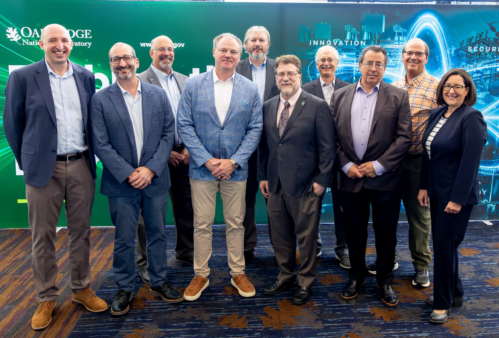 Group photo of Oak Ridge National Laboratory leaders and partners standing together in front of an ORNL-branded backdrop during an event.