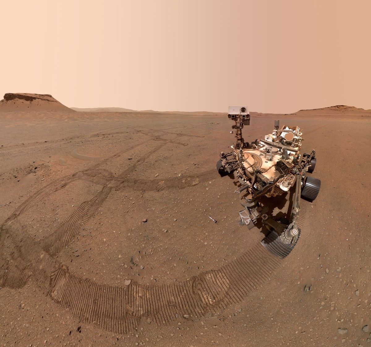 Perseverance rover on the rocky surface of Mars, surrounded by wheel tracks.
