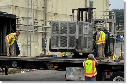 Workers unload a large radioisotope thermoelectric generator from a flatbed truck.