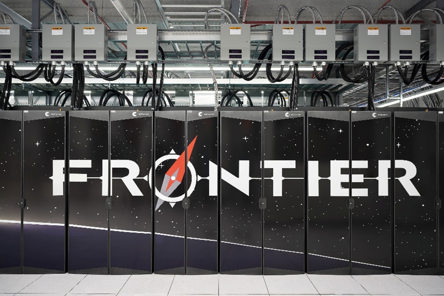 Rows of tall black computer cabinet panels display the word “FRONTIER” in a space-themed design with stars and a compass emblem. Overhead, power and cooling equipment and cables hang in an industrial data-center environment.